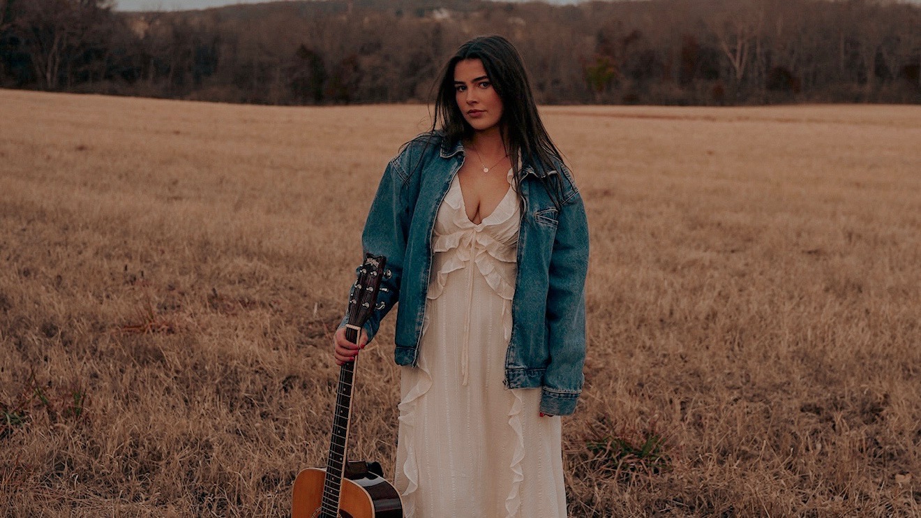 Kailey Jane standing in a field with her guitar at golden hour