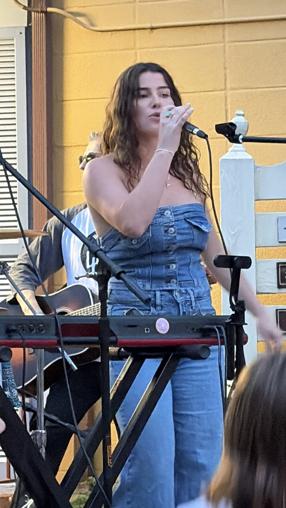 Kailey Jane singing into the mic with her band behind her at GIGS Courtyard in Kensington, Maryland